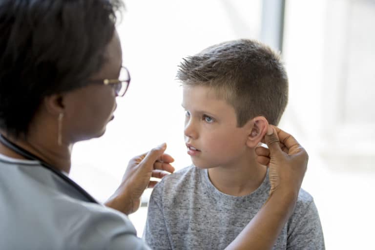 Medical Checkup A little boy is sitting on an examining table in a doctors office - a healthcare professional is implanting a hearing aid for the child.