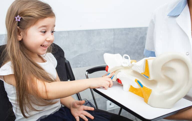 Pediatric Hearing Appointment Young girl pointing at a model of an ear in their doctor's office