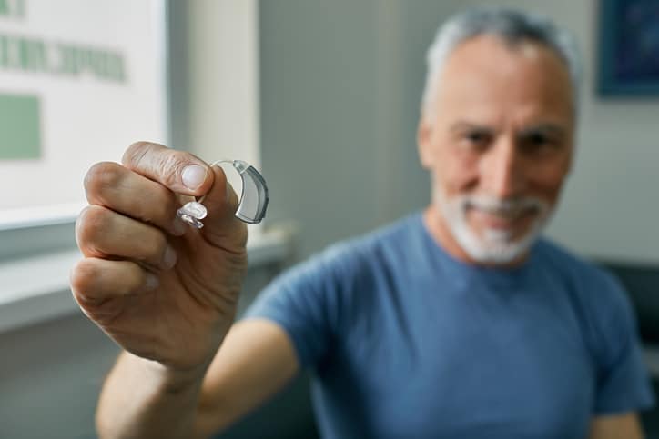 older man holding hearing aid to help with tinnitus Senior man holding BTE hearing aid in hand on foreground, close-up. Treatment of deafness in elderly people