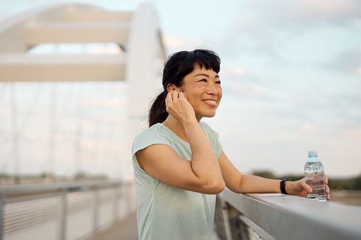 Smiling woman out for a walk crossing a bridge and adjusting her hearing aids. Smiling woman out for a walk crossing a bridge and adjusting her hearing aids.